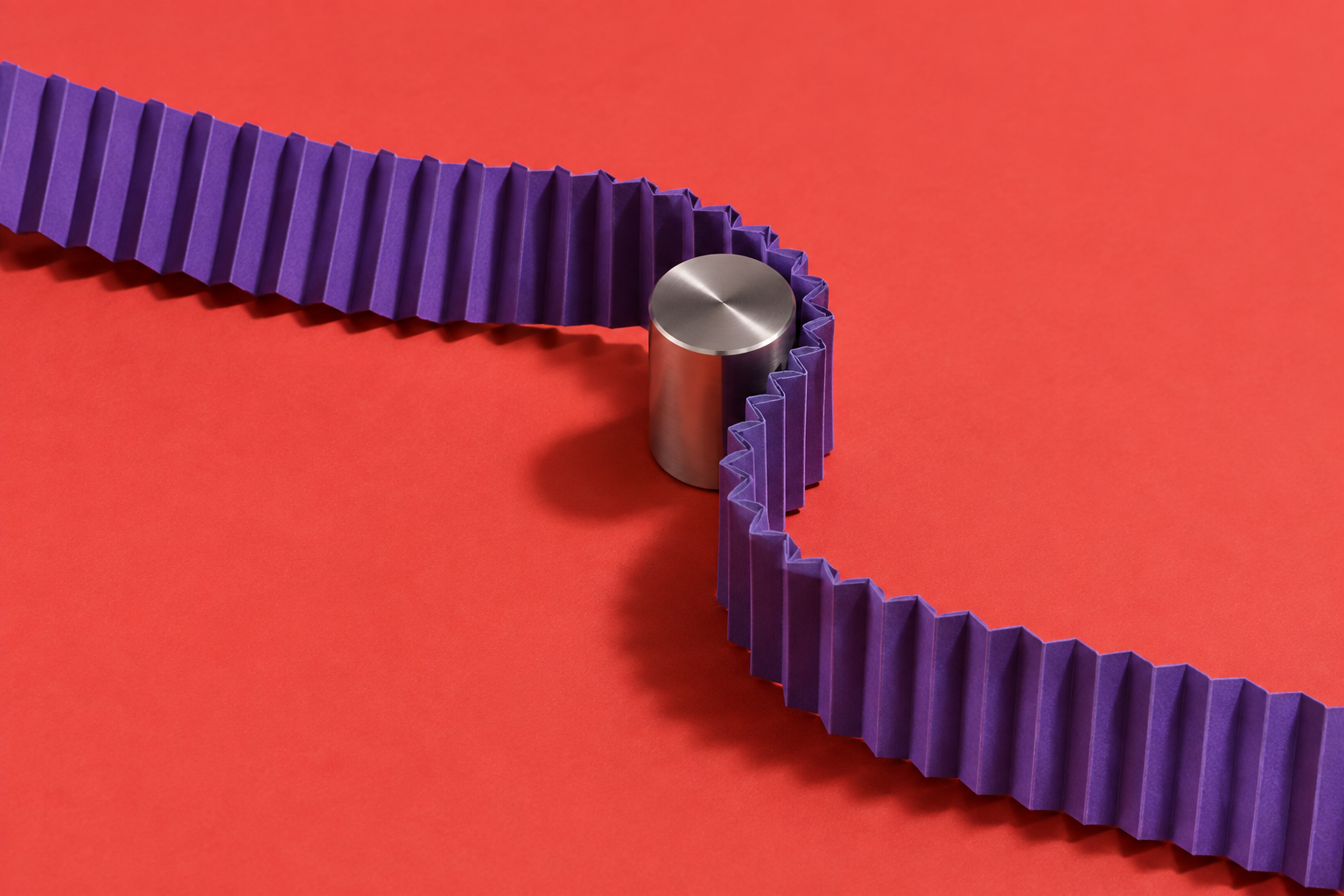 A violet folded-paper ribbon bends around a metal cylinder on a coral surface.